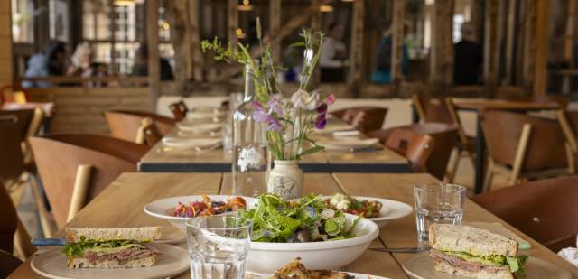 A wooden table set for lunch with plated food and glassware, at Knepp kitchen in Sussex