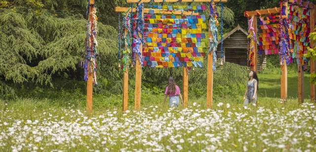 Two women look at a multi coloured art installation in a wildflower meadow, at Wakehurst gardens