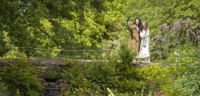 Two women stand on a bridge taking a selfie, in Wakehurst gardens in Sussex