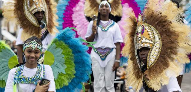 Children dressed in carnival and masquarade costumes, posing for the camera. With large featured and multi coloured head wear.