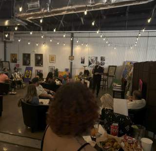 Guests enjoying a poetry reading at a local venue in Fayetteville, NC, with string lights and artwork on display.