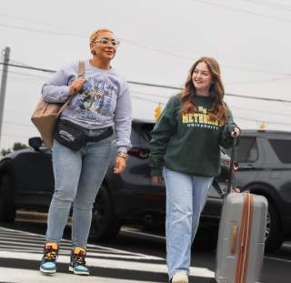 Two travelers smiling as they cross a street with luggage on their way to a hotel in Cumberland County, North Carolina.