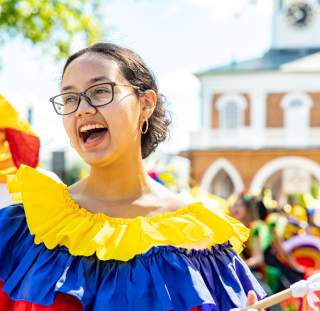 Performer in colorful yellow, red, and blue folkloric attire smiling joyfully in front of the iconic Market House during Fayetteville’s International Folk Festival.