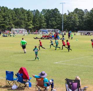 Youth soccer games in progress across multiple outdoor fields with teams playing simultaneously and spectators seated along the sidelines.