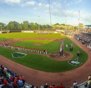 Fans filling Segra Stadium in Fayetteville, NC, for a baseball game as players line up on the field during the national anthem.