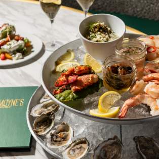 A tower of plates containing shrimp, oysters and seafood on ice with lemon and two glasses of white wine