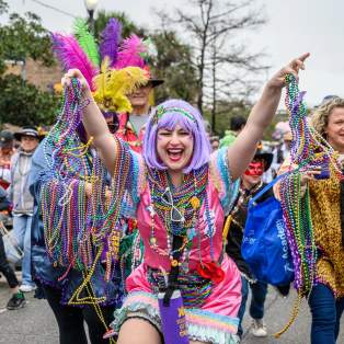 Woman in Mardi Gras costume holding beads and smiling
