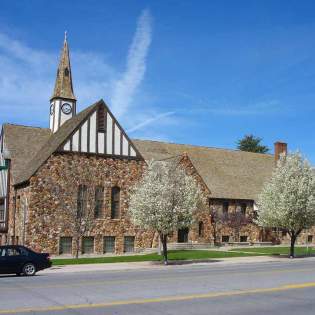 Historic stone church in Cedar City, Utah, featuring a clock tower and spring trees in bloom along a quiet street