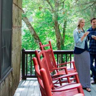 Man and woman holding cups on porch of cabin