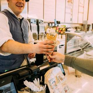 Colonial dressed ice cream shop worker hands ice cream to customer