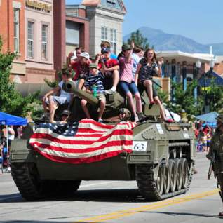 Freedom Festival parade tank going down road with American flag on it and riders on it