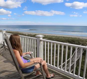 a girl sitting on a rocking chair on a deck of a vacation rental house on the beach