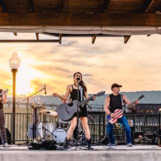 Female lead singer and her band perform at sunset on an open-air stage.