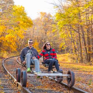 A couple peddles on a rail bike riding along the rail line in the fall.