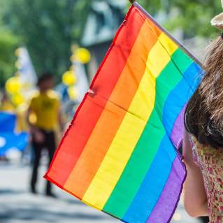 Back view of a person holding the rainbow flag over their shoulder