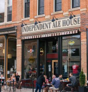 Street view of Independent Ale House, a brick building with large windows. Customers dine outside, creating a lively, friendly atmosphere.