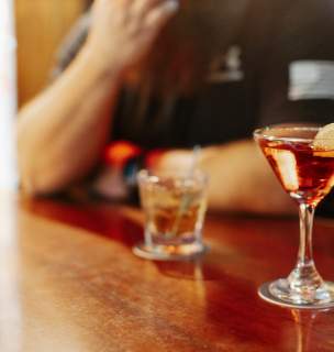 Cocktail and mixed drink sitting on bar top.