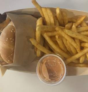 A closeup shot of a smashburger wrapped in brown paper with crip fries next to it in a basket.