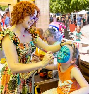 Little girl sitting on a chair getting her face painted blue