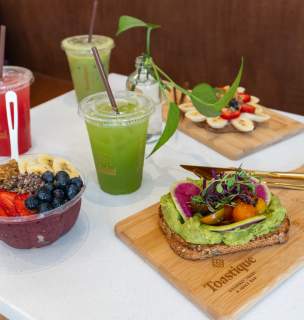 Spread of avocado toast, acai bowl, green juices, and smoothies on a white table at Toastique.