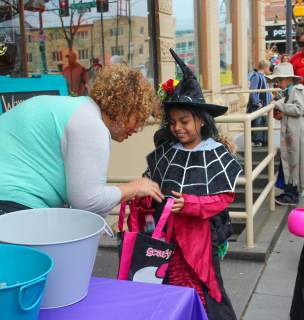 Child dressed in a witch costume collecting candy from a downtown business owner as part of the Downtown Trick-or-Treat event in Rapid City, SD.