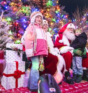Children smiling under a lighted tree with Mr. and Mrs. Claus