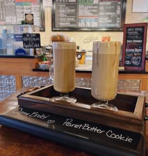 Two lattes sitting on a counter with ordering counter in the background.