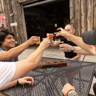 A group of adults sit around a table, holding up glasses of beer to cheers eachother.