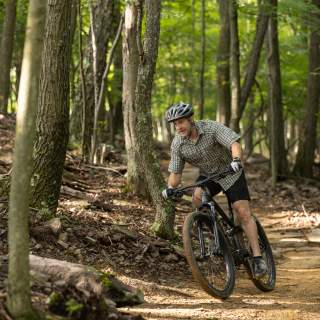 A man rides a bike on a rough mountain trail through the woods.