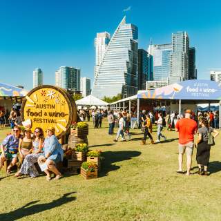 Image of people attending the Austin Food + Wine Festival at Auditorium Shores with the downtown skyline in the background.
