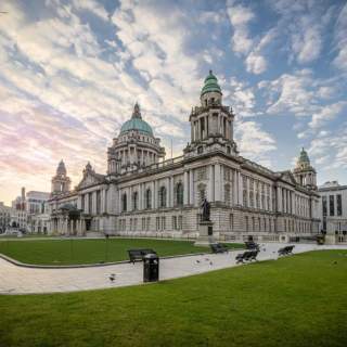 Photo of Belfast City Hall from outside looking at the grass areas and benches.