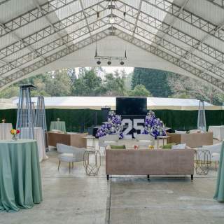 high tabletops with blue linens, benches, and heaters are inside a massive tent