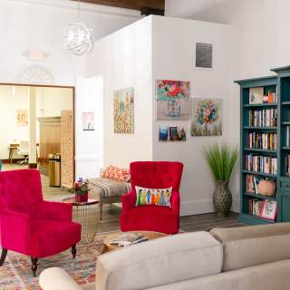 Pink armchairs and a blue bookcase make a cozy library space with colorful artwork on the walls