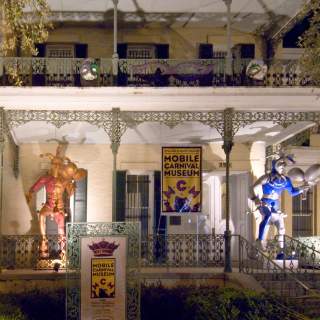 Historical, white house with iron columns and trim, two Mardi Gras Jesters on the porch