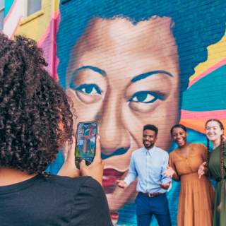 3 Friends Pose in front of Street Art mural while a person takes a photo
