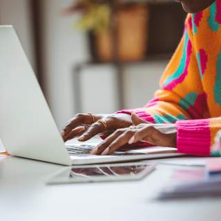 A person wearing a vibrant, colorful sweater types on a laptop.