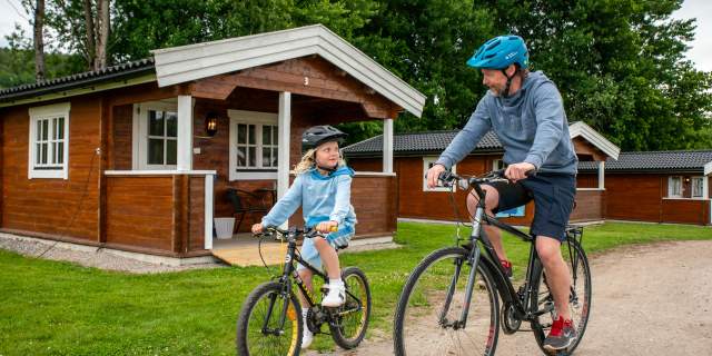 En mann og en jente på sykkel foran en camping hytte.