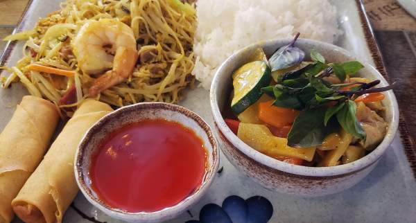 Thai-style meal with shrimp noodles, white rice, fresh vegetables, spring rolls, and sweet chili sauce