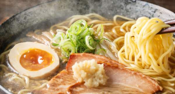Steaming bowl of ramen with noodles, soft boiled egg, pork, and green onions in savory broth