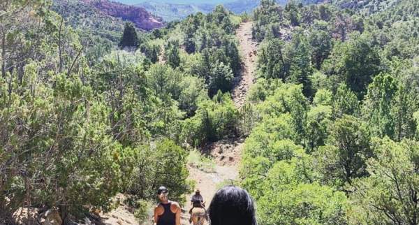 Horseback riders traveling along a scenic mountain trail surrounded by forests and red rock hills near Cedar City, Utah