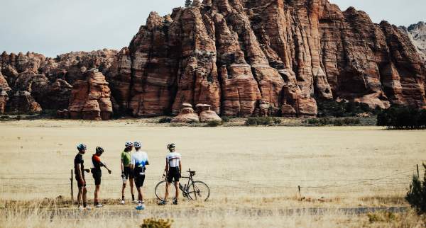 Five cyclists stand in front of a red rock formation in Kanarraville, Utah.