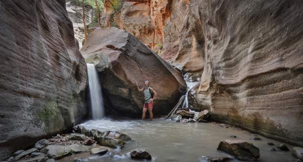 Woman standing beside a waterfall within a red rock slot canyon in southern Utah.