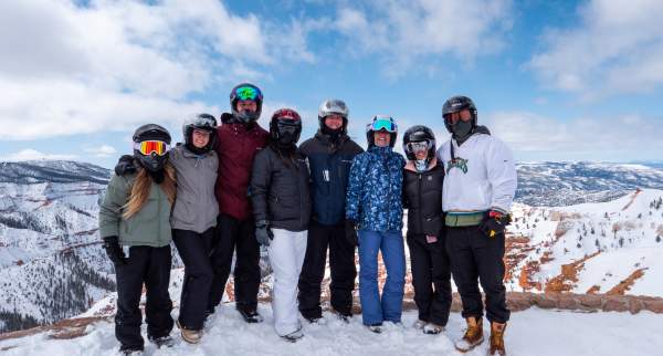 A group of eight adults dressed for winter recreation stand together for a photo at the North Overlook of Cedar Breaks National Monument