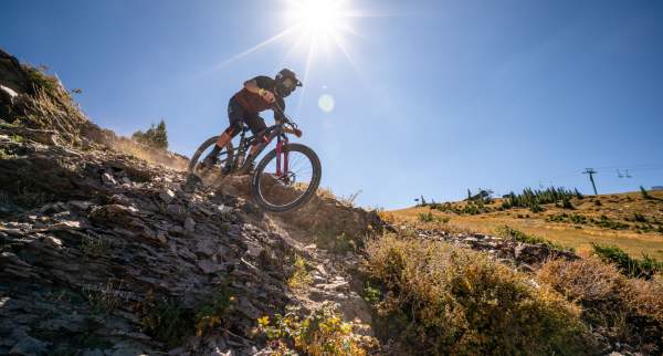 Mountain biker descending rocky trail under bright sun at Brian Head with scenic alpine landscape