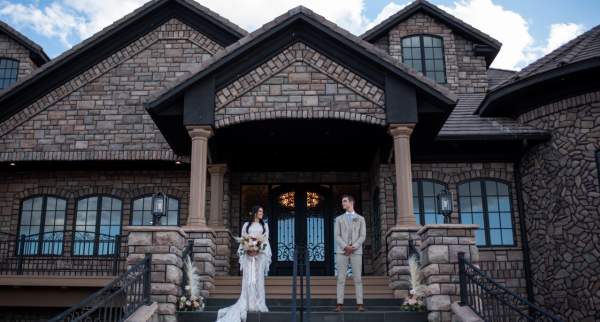 Couple stands on the front porch of the Cedar Rose Estate wedding venue in Parowan, Utah.