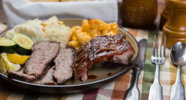 BBQ plate with ribs, sliced brisket, mac and cheese, potatoes, and bread served at a rustic table