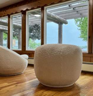 Two cream retro themed chairs in front of a floor to ceiling windows over looking a lake.