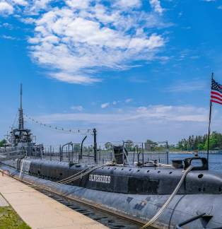 world war II submarine docked in channel. blue skies with white clouds, american flag flying