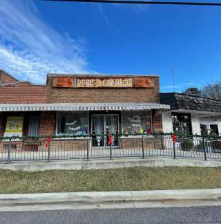 Old brick building with a sign that says Doris McDaniel, decorated for Christmas with window paintings and garland with red bows on the railing