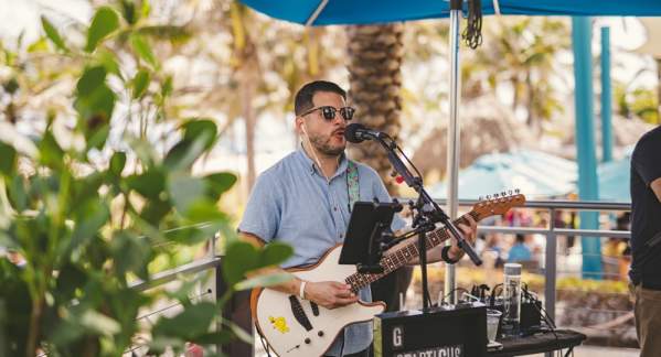 Man playing a guitar under a blue umbrella on the patio of Oceanic